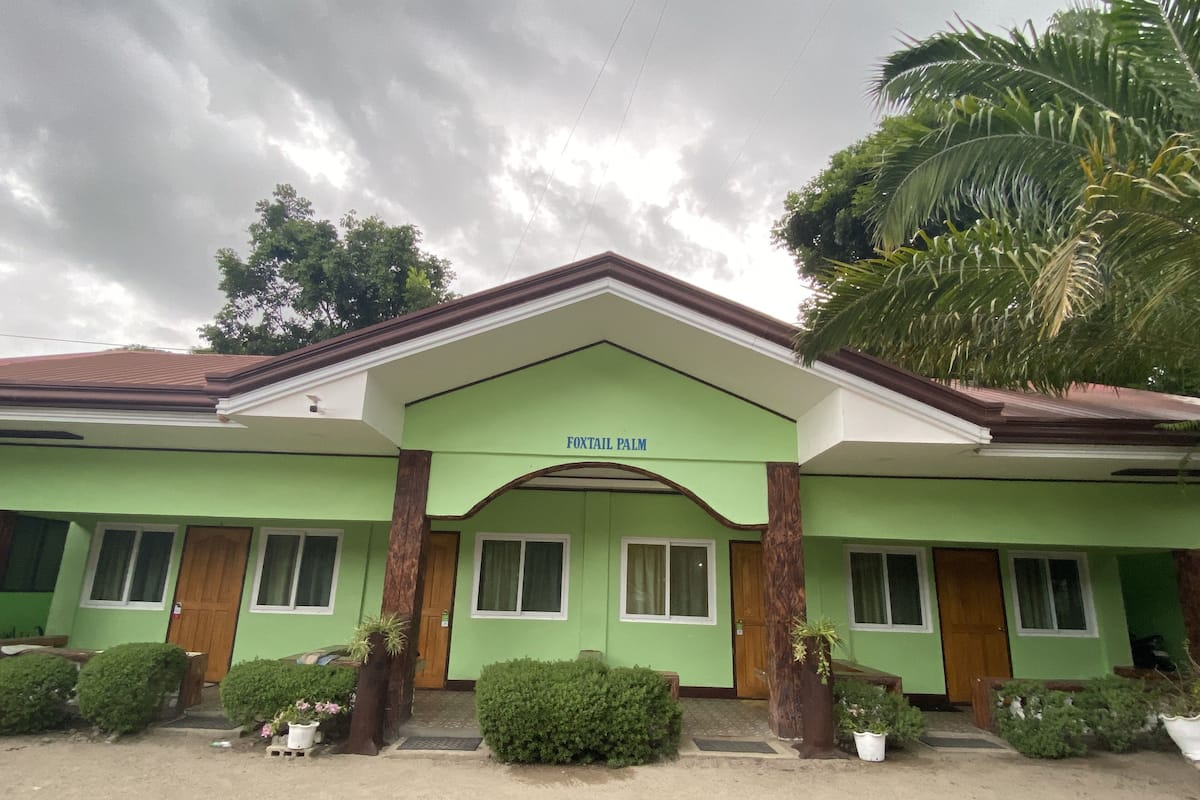 A building with a green facade, a sign reading "FOXTAIL PALM", and a covered entrance with columns.