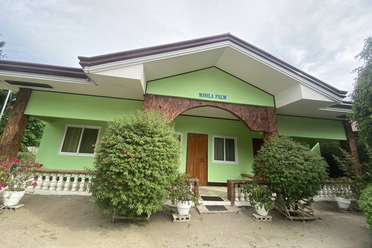 A building with a green facade, a wooden door, and a sign reading "MANILA PALM".