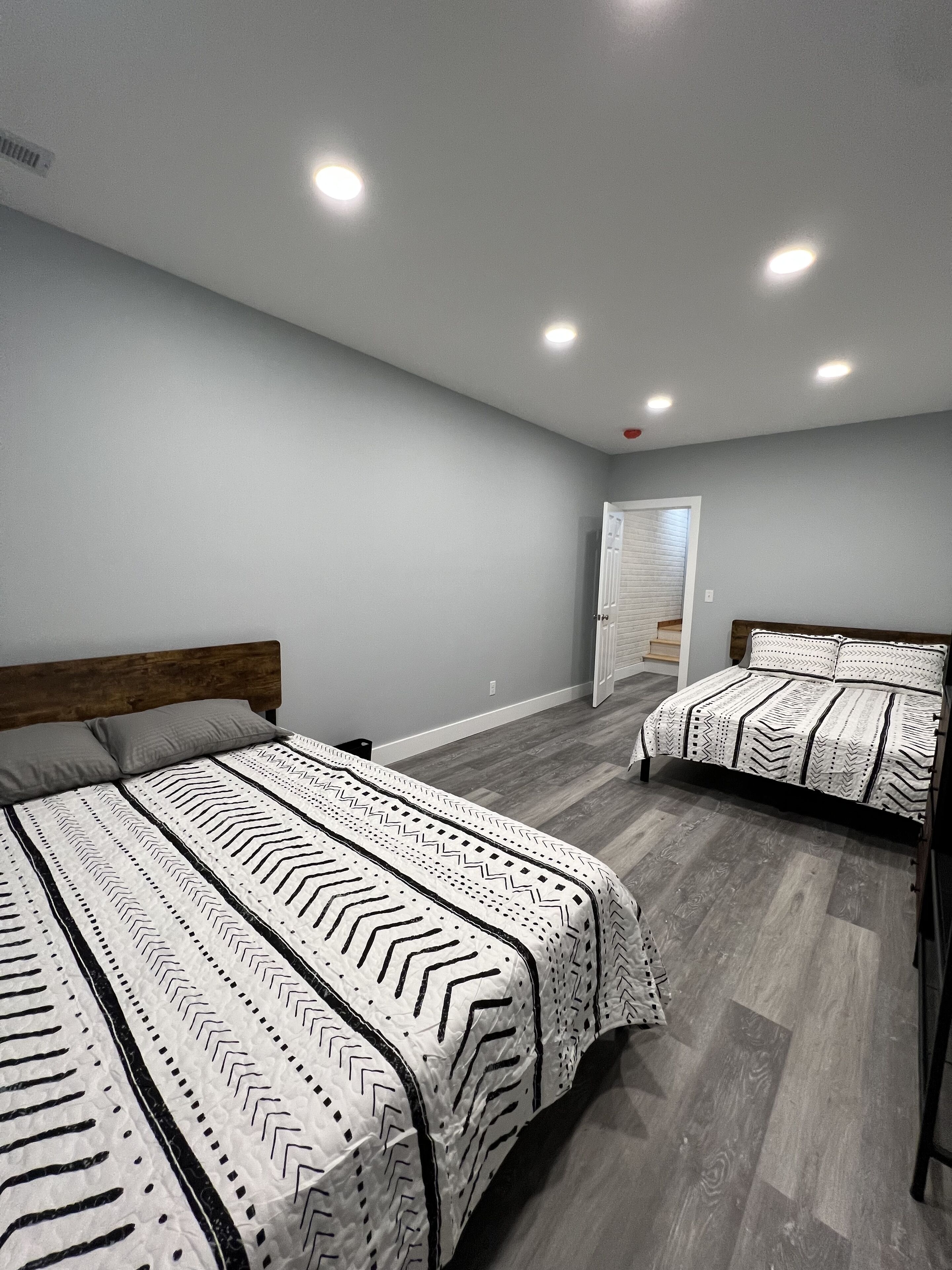 Une chambre avec deux lits, des murs gris et un plancher en bois.
