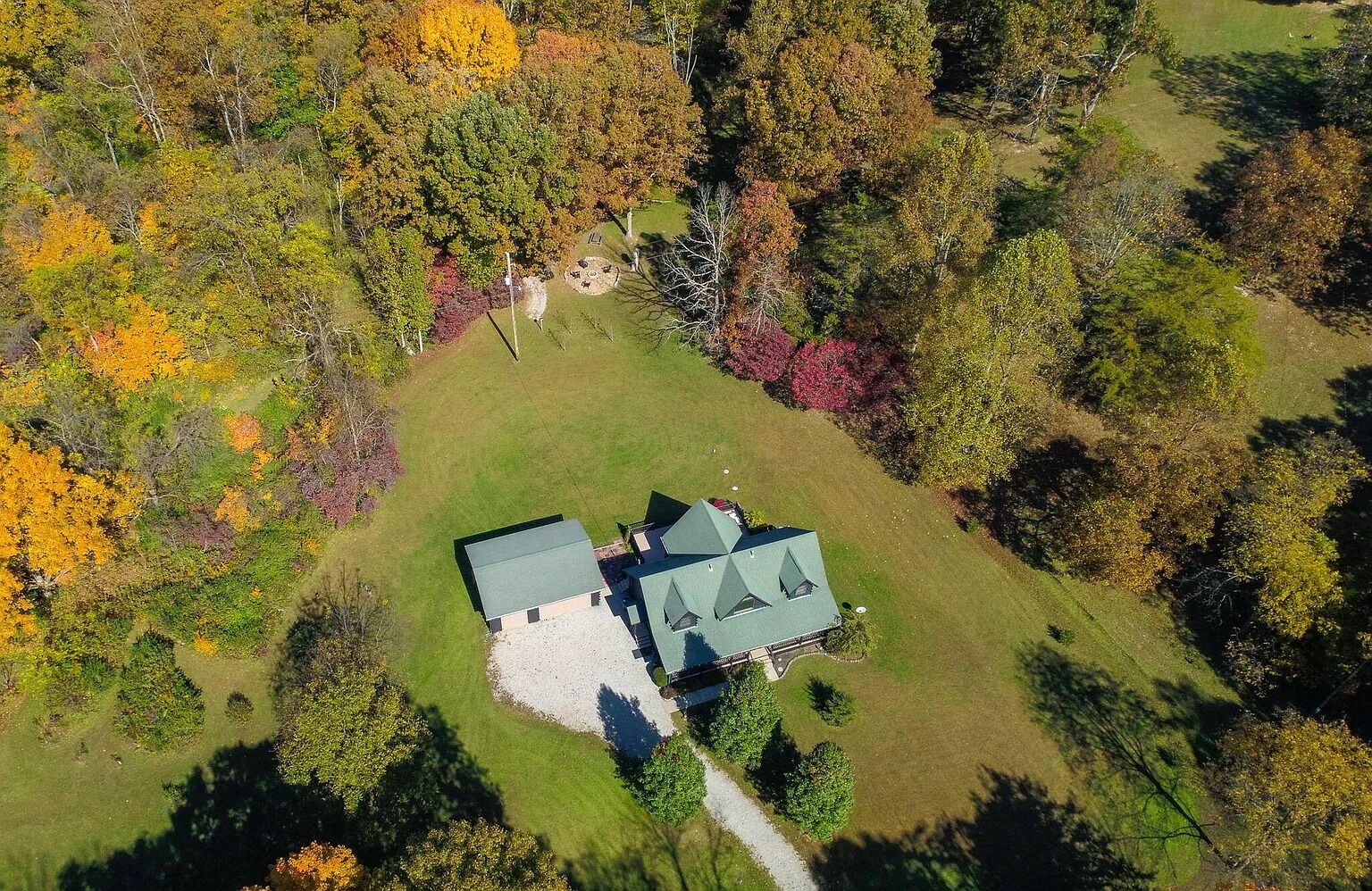 Eine Vogelperspektive zeigt ein Haus mit einem begrünten Dach, umgeben von einer gepflegten Rasenfläche und dichten Bäumen im Herbstlaub.