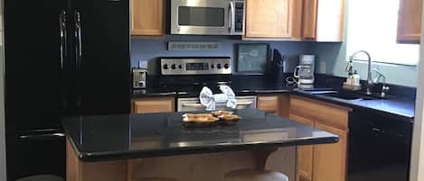 A kitchen with wooden cabinets, a black refrigerator, a microwave, a stove, and a sink. There are two stools at the kitchen island.