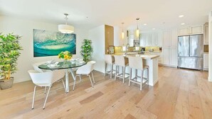 Een moderne keuken met witte kasten, roestvrijstalen apparatuur en een eethoek met een glazen tafel en witte stoelen.
