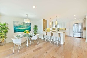 A modern kitchen with white cabinets, stainless steel appliances, and a dining area with a glass table and white chairs.