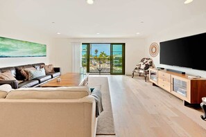 A modern living room with a sofa, coffee table, TV, and a view through a large window.