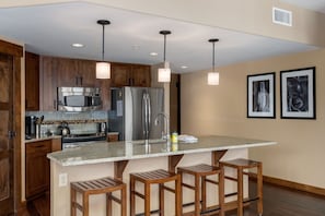 Una cocina moderna con armarios de madera, electrodomésticos de acero inoxidable y una isla central con taburetes de bar.