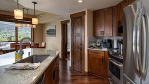 Une cuisine moderne dotée d’un réfrigérateur en acier inoxydable, de plans de travail en granit, d’armoires en bois et d’une grande fenêtre offrant une vue panoramique.