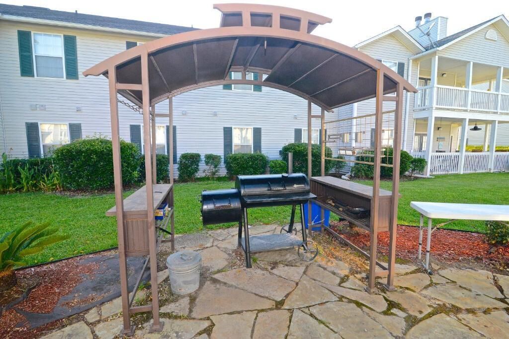 Een terras buiten met een barbecue en zitgedeelte, stenen vloer en een overdekte constructie.