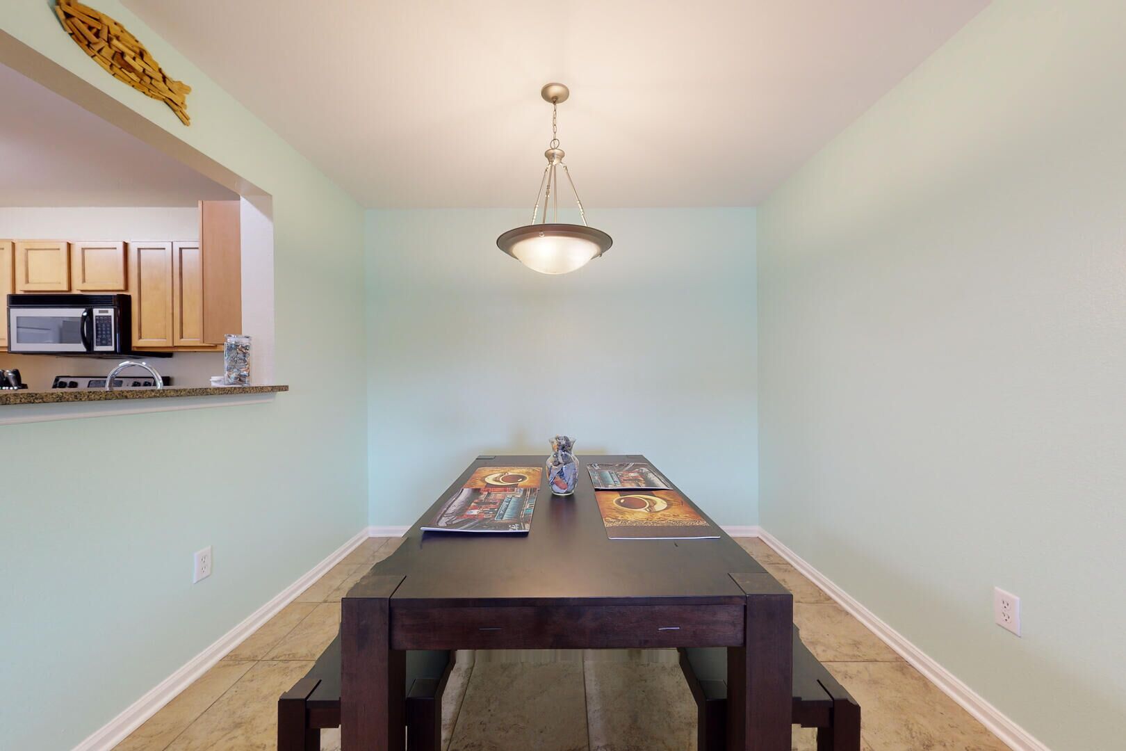 A dining area with a dark wooden table, light blue walls, and a hanging light fixture.