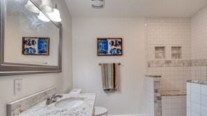 Un baño con lavabo de mármol, inodoro, ducha con pared de mármol y dos obras de arte enmarcadas en la pared.