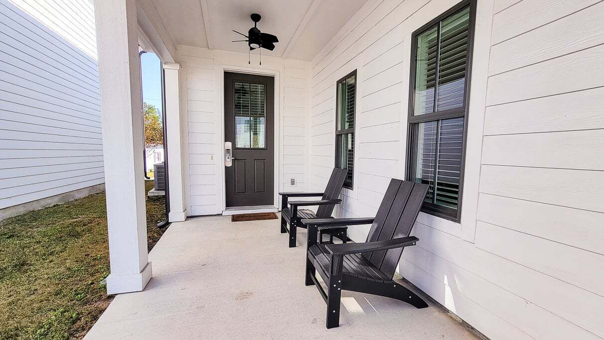 Une véranda avec deux chaises noires, une porte blanche et un ventilateur de plafond.