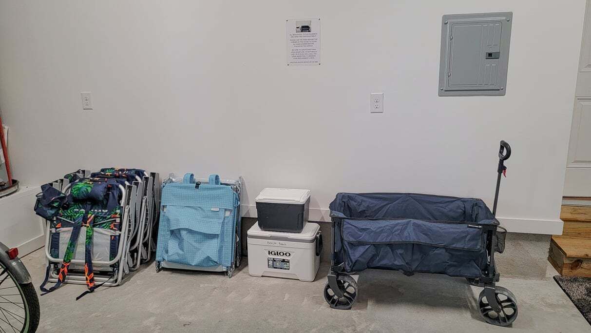 A wheelchair, a blue suitcase, and a storage box in a room with white walls and a door.
