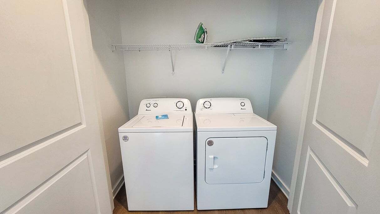 A laundry room with two white front-loading washing machines and a small shelf above them.