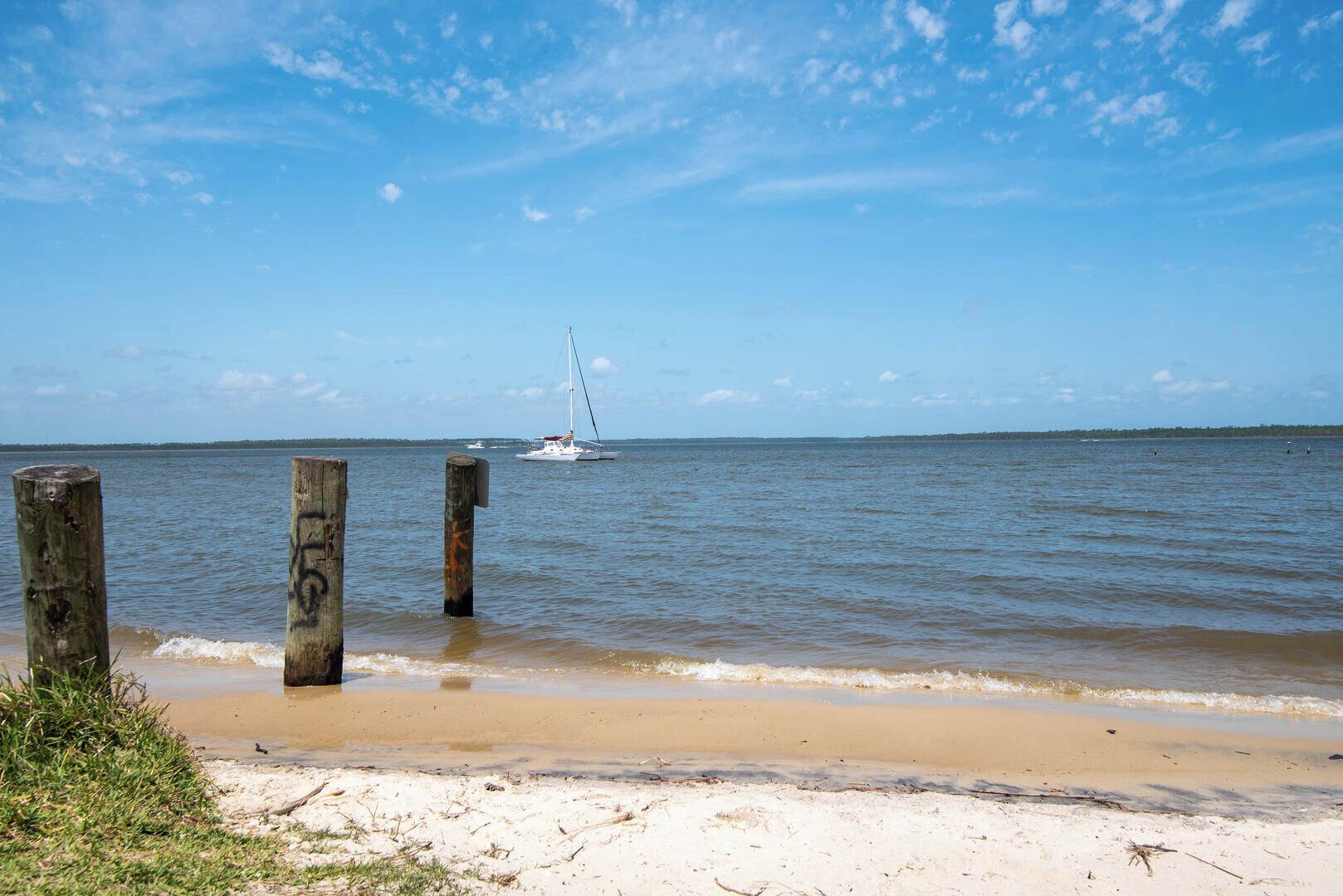 Ein Strand mit Holzpfählen, einem sandigen Ufer und einem Segelboot in der Ferne.