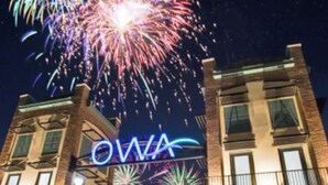 Um edifício com um letreiro de neon que diz "OWA" e um céu noturno com fogos de artifício.