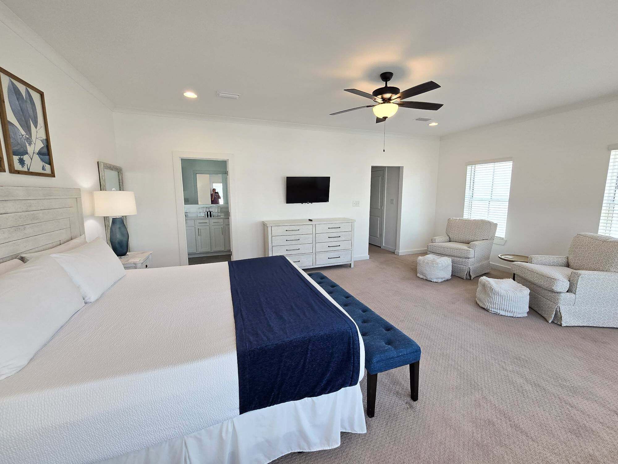 A bedroom with a bed, a desk, a chair, a TV, and a ceiling fan.
