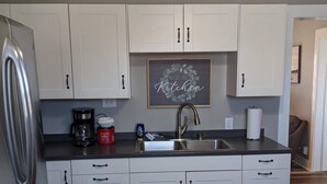 A modern kitchen with white cabinets, a stainless steel refrigerator, a coffee maker, and a sink. - Farmhouse on the Prairie - You can see for miles! (valley falls)