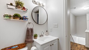 Une salle de bain avec un lavabo blanc, un miroir et des étagères contenant des articles de toilette.