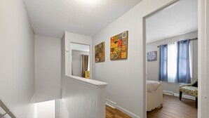 Un escalier menant à une chambre à coucher qui contient un lit, une chaise et une fenêtre avec des rideaux.