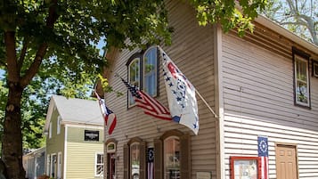 A historic building with American flags, a wooden porch, and a brick pathway.