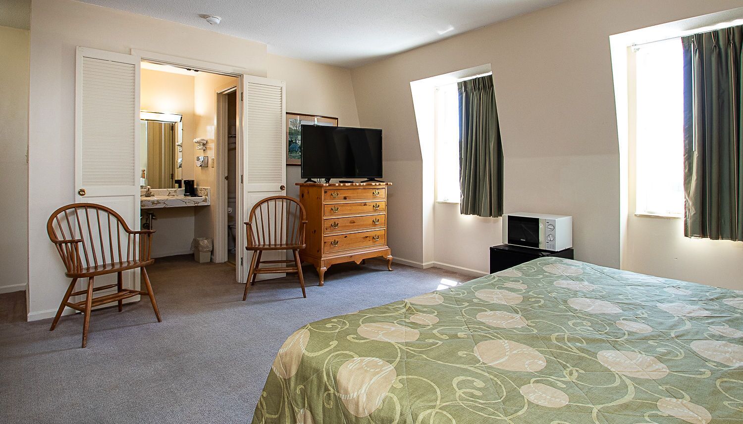 A bedroom with a bed, dresser, chairs, a television, and a microwave.