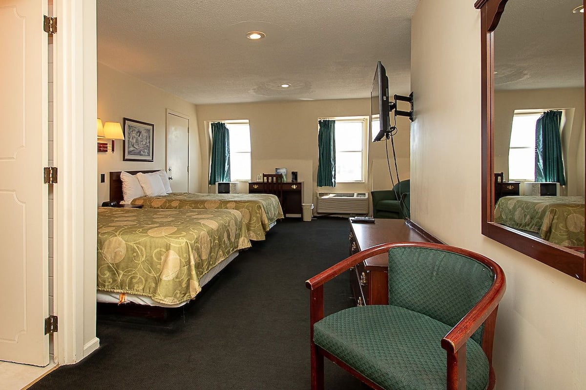 A hotel room with two beds, a desk, a chair, a TV, and a large mirror.
