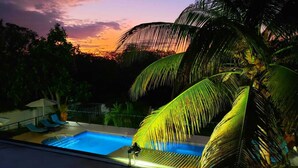 A swimming pool with lounge chairs and umbrellas, surrounded by palm trees and a sunset view. - 🏝️ Forever Summer | Gorgeous 4BDR Villa w/ Pool - Panoramic Views (Runaway Bay)