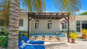 A covered outdoor seating area with blue lounge chairs, a small table, and a potted plant. - 🏝️ Forever Summer | Gorgeous 4BDR Villa w/ Pool - Panoramic Views (Runaway Bay)