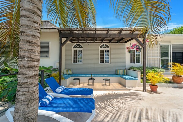 A covered outdoor seating area with blue lounge chairs, a small table, and a potted plant.