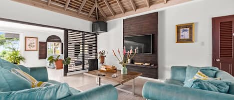 Amplia sala de estar con techo de madera alta, televisor grande y sofás color turquesa.