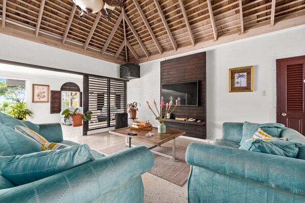 Amplia sala de estar con techo de madera alta, televisor grande y sofás color turquesa.
