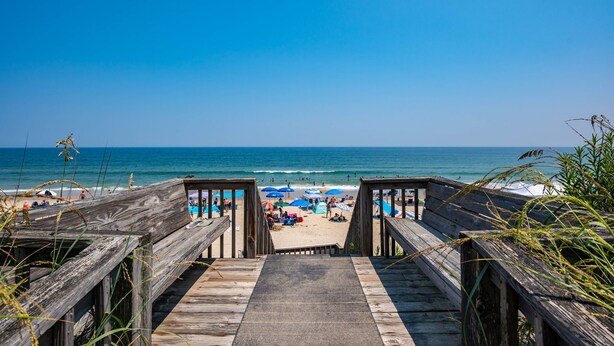 A wooden boardwalk leading to a beach with umbrellas and beachgoers. - Off Crew-Oceanfront, pool, hot tub, private walkway to the beach, game room, ocean views! (Corolla)