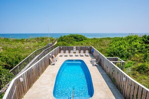 A rectangular pool with a wooden deck and lounge chairs, surrounded by a wooden fence, with a view of the ocean. - Off Crew-Oceanfront, pool, hot tub, private walkway to the beach, game room, ocean views! (Corolla)