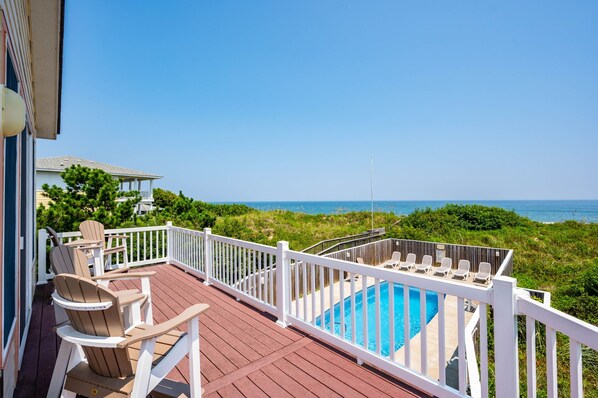 Une terrasse en bois avec une piscine, des rampes blanches et une vue sur la plage.