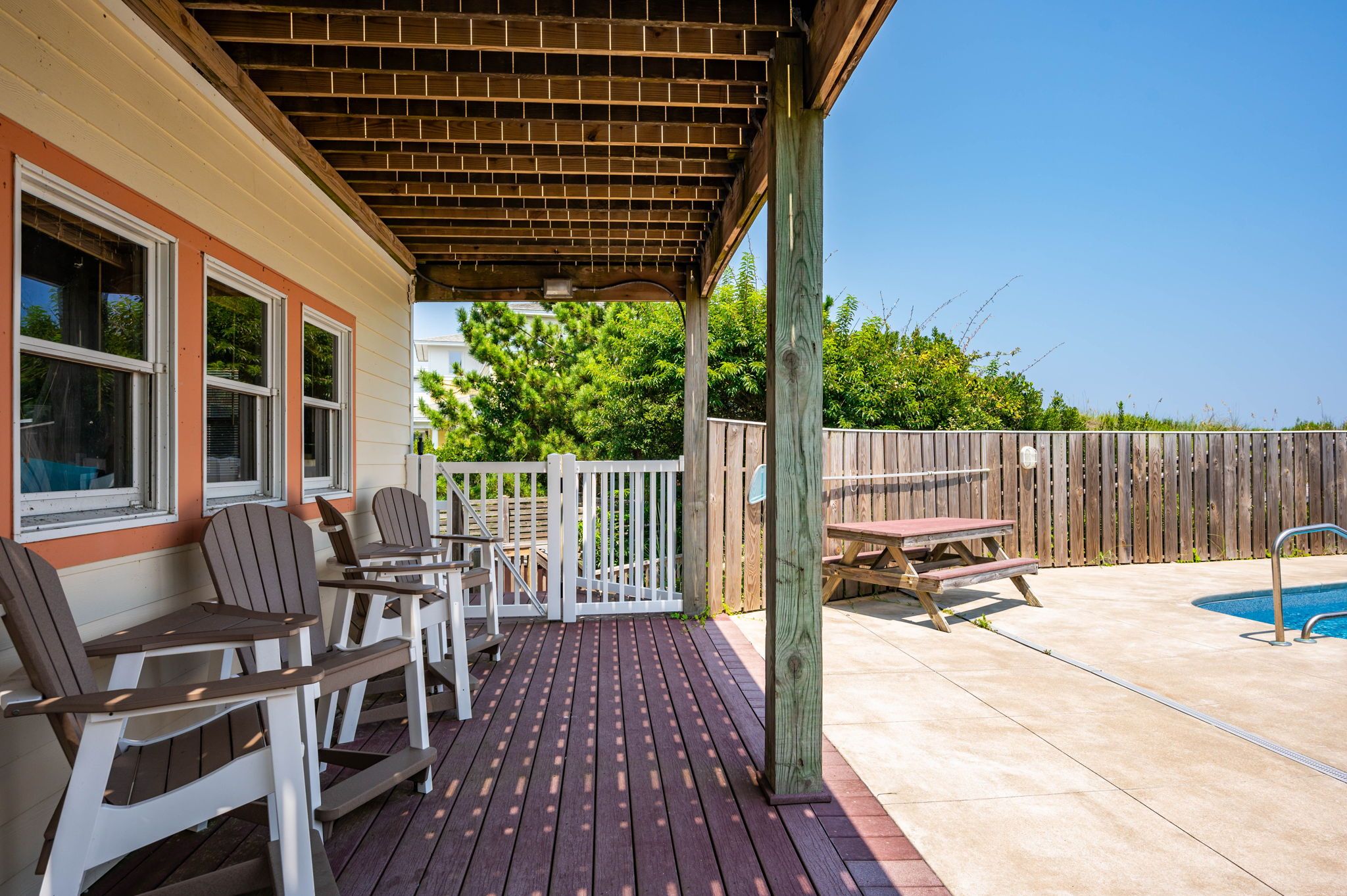 Une terrasse couverte avec des sièges d’extérieur, une piscine et une clôture en bois.
