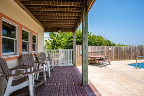 Une terrasse couverte avec des sièges d’extérieur, une piscine et une clôture en bois.