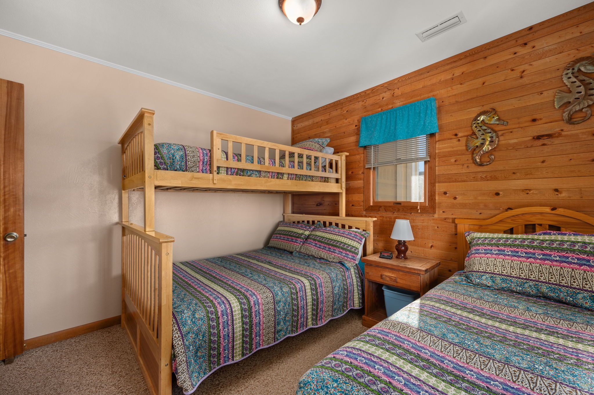 A room with two bunk beds, a desk, a lamp, and a window with blinds.