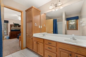 A bathroom with a double sink vanity, wooden cabinets, a large mirror, and a shower area.