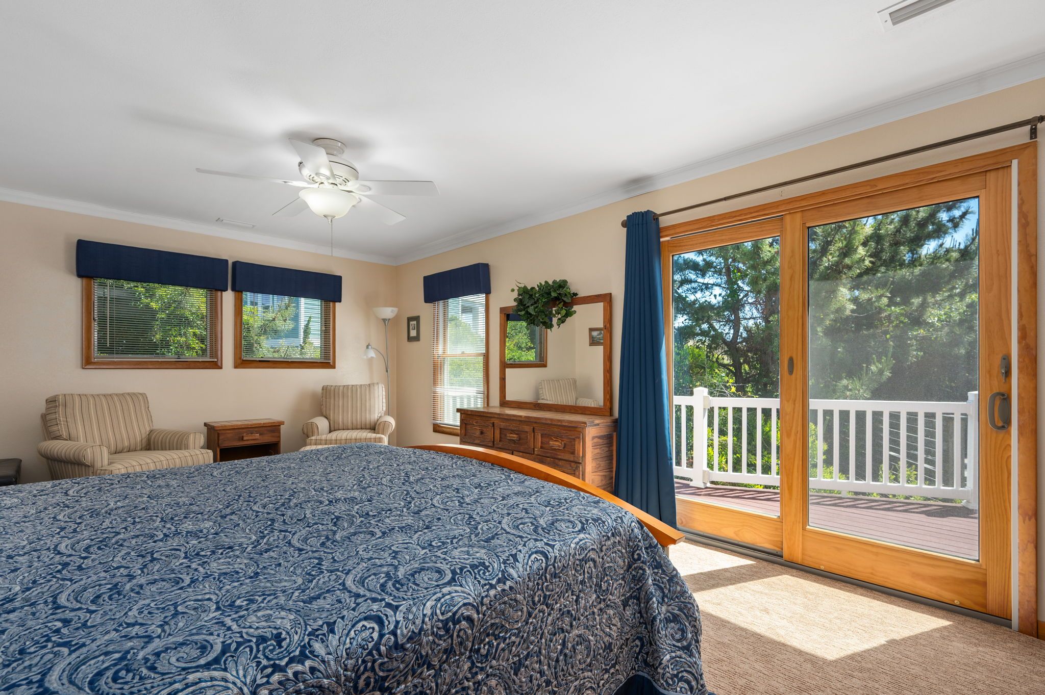 A bedroom with a large bed, a desk, a chair, a dresser, and a sliding glass door leading to a balcony.