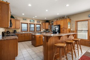 Una cocina con armarios de madera, una isla central con taburetes, un refrigerador y un microondas.