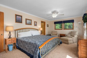 A bedroom with a bed, a chair, a desk, a lamp, a ceiling fan, and framed pictures on the wall.