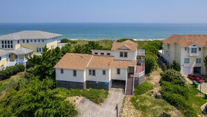 A coastal residential area with houses, a clear view of the ocean, and a paved driveway leading to a garage. - Off Crew-Oceanfront, pool, hot tub, private walkway to the beach, game room, ocean views! (Corolla)