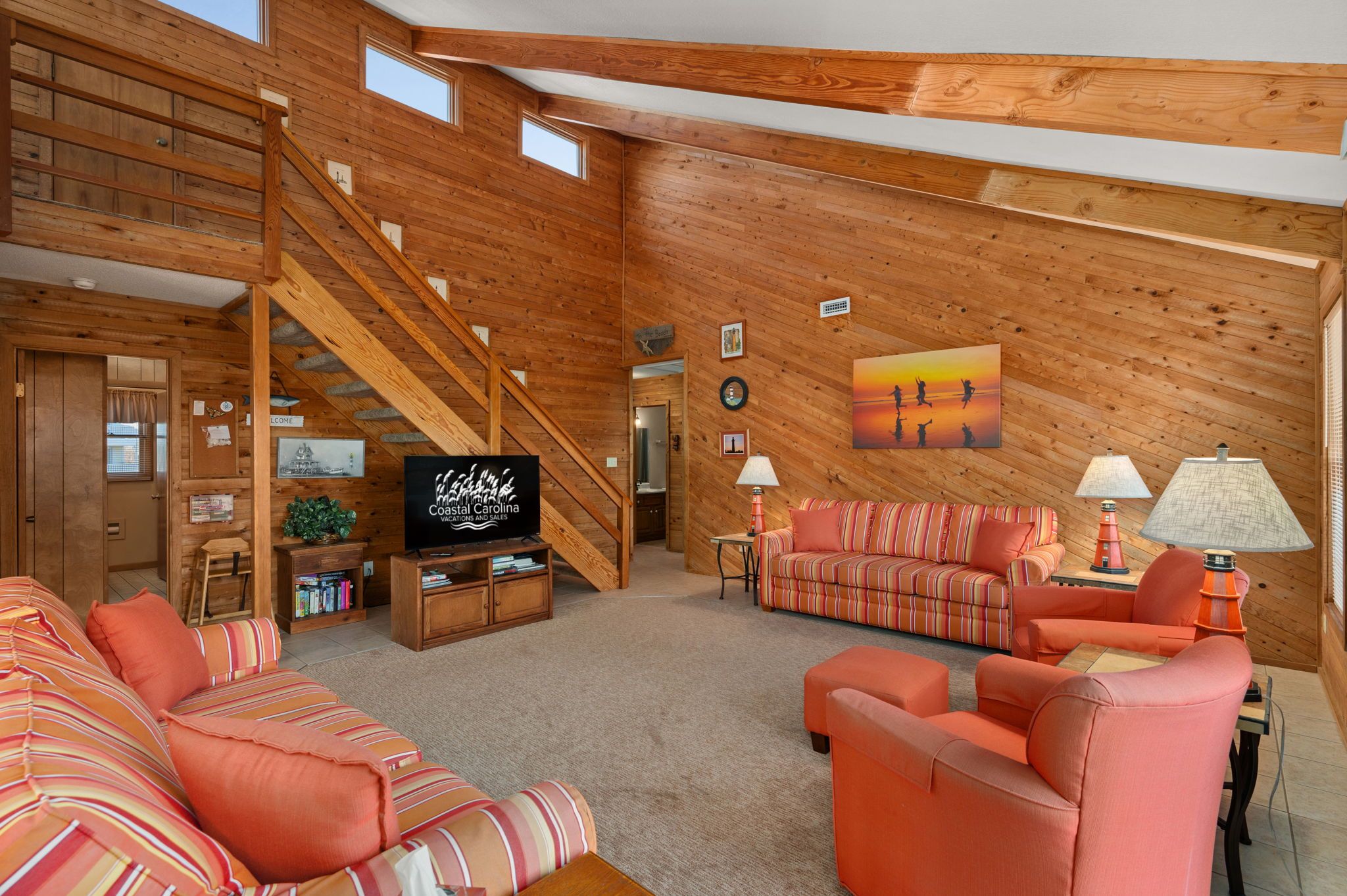 Un vaste salon au décor intérieur en bois, avec un escalier, un téléviseur et un grand tableau accroché au mur.