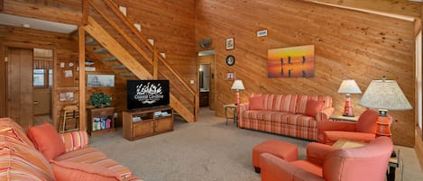 Ein geräumiges Wohnzimmer mit Holzvertäfelung, einer Treppe, einem Fernseher und einem großen Gemälde an der Wand.