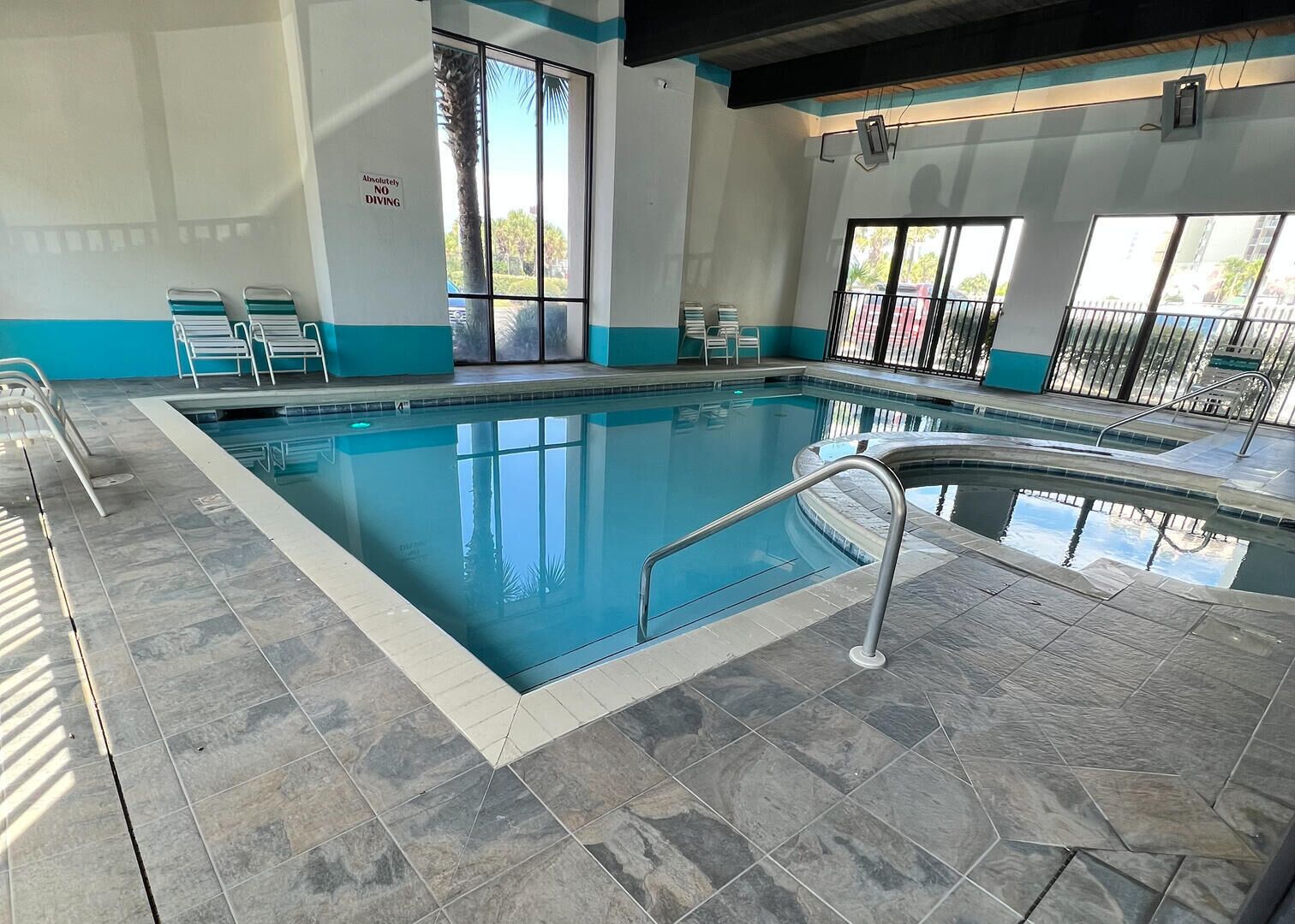Une piscine intérieure à l’eau claire, avec un revêtement de sol carrelé et un panneau indiquant qu’il est interdit de plonger.