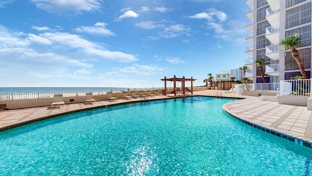 A pool area with a clear view of the ocean, a pergola, and a building with balconies. - Stunning Views, 3bd/2ba w/ Private Balcony (Orange Beach)