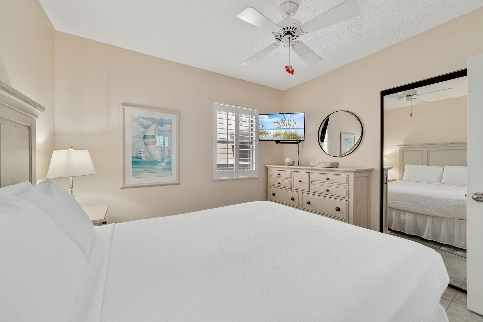 A bedroom with a bed, a dresser, a television, a ceiling fan, a framed picture, and a mirror.