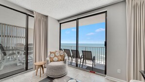 A balcony with a view of the ocean, a round grey armchair with star-patterned cushions, and a small wooden table. - Stunning Views, 3bd/2ba w/ Private Balcony (Orange Beach)