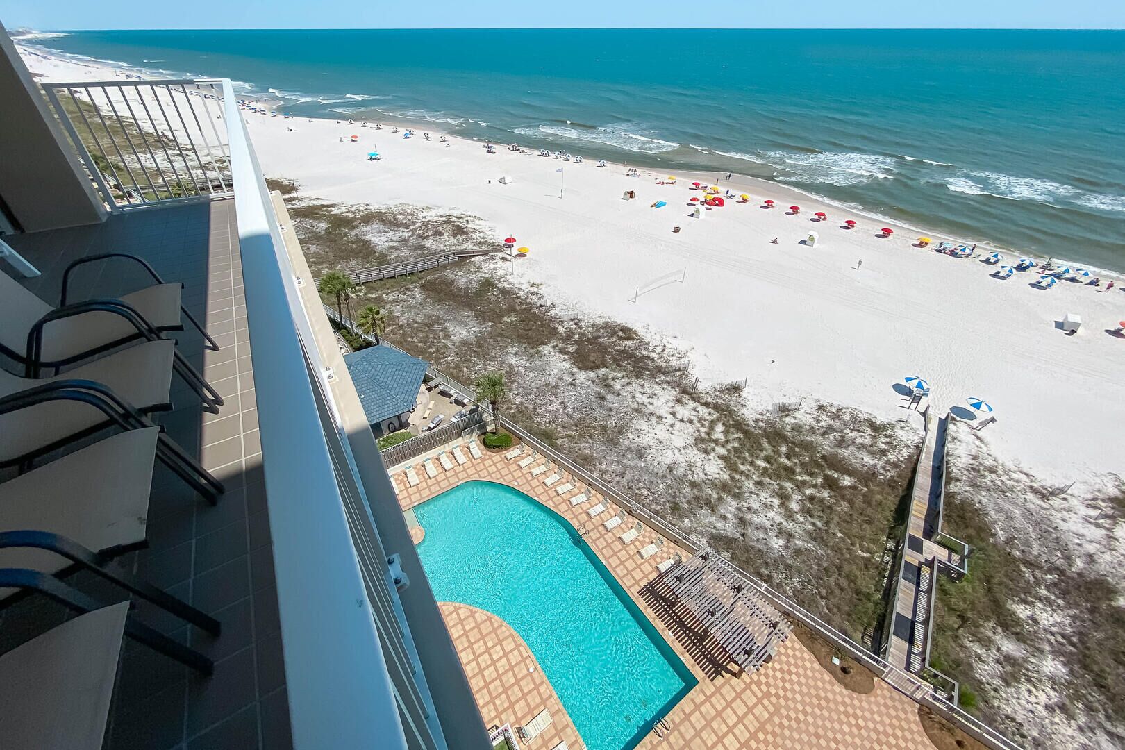 A hotel balcony with a view of a beach and a swimming pool.