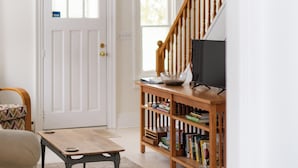 A hallway with a white door, a small table, a bookshelf, and a staircase. - The Poplars Suite 1827: A Historic Stay (Cobourg)