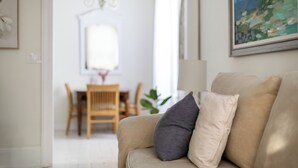 A living room with a beige sofa, a chandelier, a dining table with chairs, and a painting on the wall. - The Poplars Suite 1827: A Historic Stay (Cobourg)